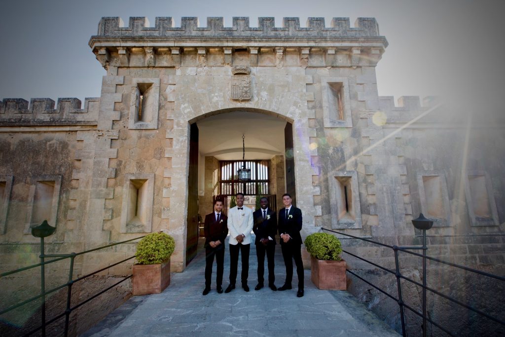 Liam-Moore-and  his groomsmen wearing bespoke wedding suits standing in front of a historic castle, highlighting the sophistication and personalized craftsmanship of custom-made wedding attire.